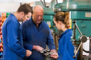 Two apprentice machinists in workspace by machine talking to trainer or manager